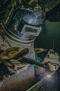 Professional welder wearing safety gear performing TIG welding on steel in a Brazilian factory.